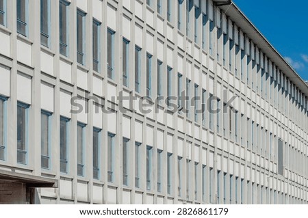 Rows of windows line a long modern industrial building facade, urban architecture scene.