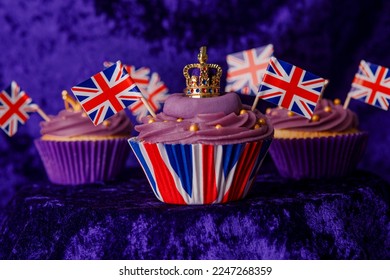 Royal Coronation Cupcakes to celebrate the coronation of King Charles III. Cupcakes decorated with the crown, purple velvet backdrop, union jacks flags, luxury cupcakes on a pedestal. 