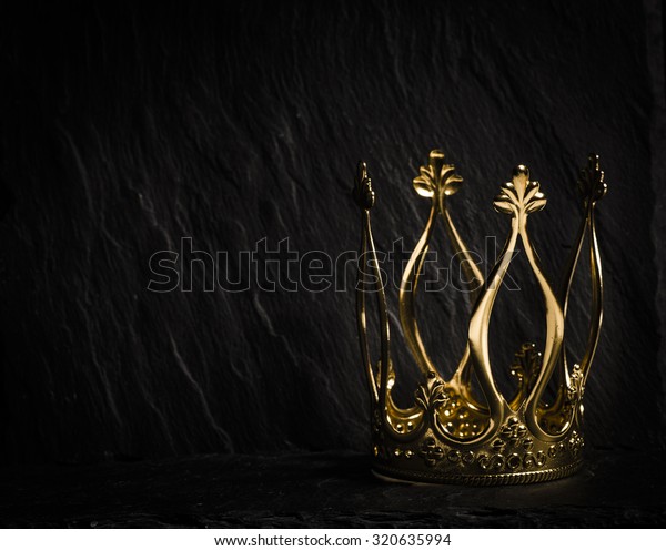 Royal gold crown on dark stone surface. Concept\
of wealth, success and\
kingdom.