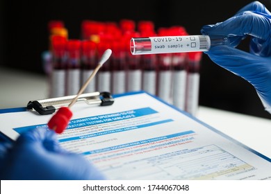 rt-PCR COVID-19 virus disease diagnostic test,lab technician wearing blue protective gloves holding test tube with swabbing stick,swab sample equipment kit and UK form specimen submitting guidelines