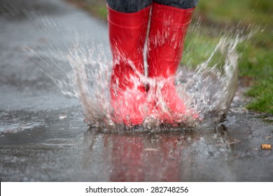 Rubber Boots Are Jumping Into A Big Puddle With Splash.