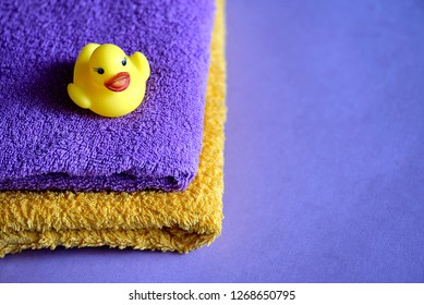 Rubber duck on a stack of terry towels on a purple background