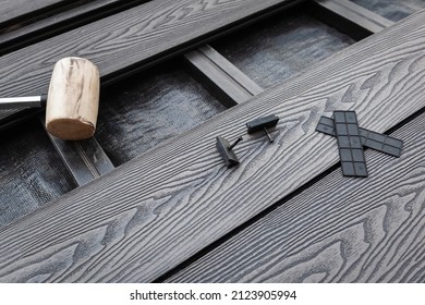 Rubber head mallet and black plastic fixings on a grey decking boards. Composite decking board installation.  - Shutterstock ID 2123905994