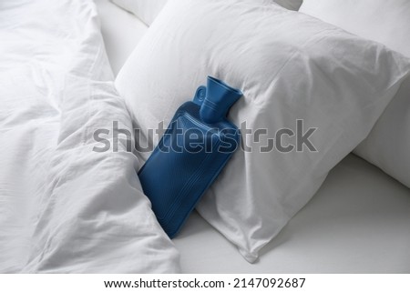 Rubber hot water bottle near soft pillow on bed