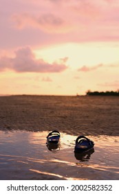 rubber shoes placed on the sea and the sandy beach at the time of the sunset. The dramatic sky is pink with orange and looks so beautiful.