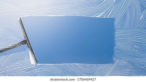 Rubber squeegee cleans a soaped window and clears a stripe of blue sky, concept for tranparency or spring cleaning, with copyspace for your individual text.