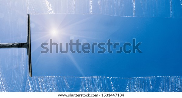 Rubber squeegee cleans a soaped window\
and clears a stripe of blue sky, concept for tranparency or spring\
cleaning, with copyspace for your individual\
text.