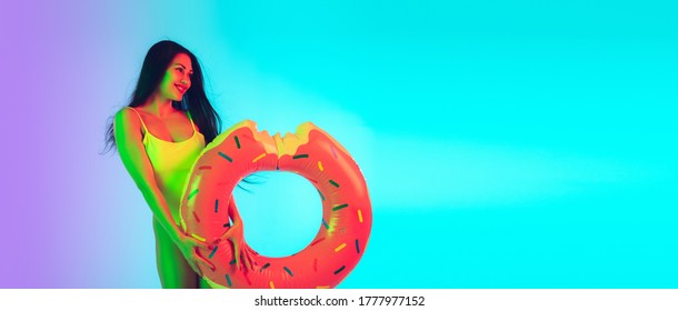 Rubber Swim Donut. Beautiful Young Girl' Portrait Isolated On Gradient Studio Background In Neon Light. Woman In Fashionable Bodysuit. Facial Expression, Summer, Weekend, Beauty, Resort Concept.