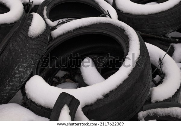 Rubber tires in the snow. Winter tires. Pile of\
old tires. Tire warehouse on the street in the snow. Unnecessary\
rubber tires.