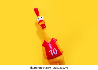 Rubber toy in the form of a rooster on a yellow background. The funny toy rooster has a surprised and dumbfounded look with its beak open. The toy makes loud noises. Free space for text