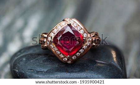 Ruby ring Surrounded by diamonds,Trillion Cut,Pink gold ring,placed on a  black pebbles.