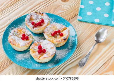 ruddy cheesecakes decorated frozen red currant berries and powdered sugar on blue plate,  blue napkin at white polka dots, old silver tea spoon on wooden table
