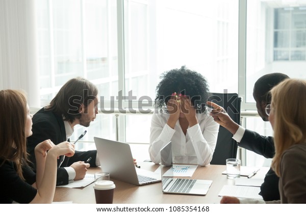 Rude diverse colleagues humiliating offending\
stressed upset young african woman leader suffering from gender\
racial discrimination during meeting or feeling exhausted tired of\
responsibility at work