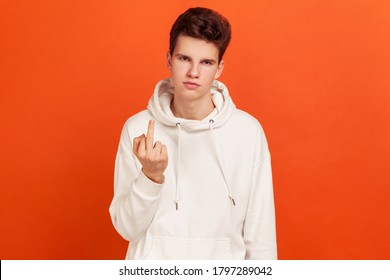 Rude Selfish Teenager In Casual White Hoodie Showing Middle Finger At Camera, Back Off, Aggression Gesture. Indoor Studio Shot Isolated On Orange Background