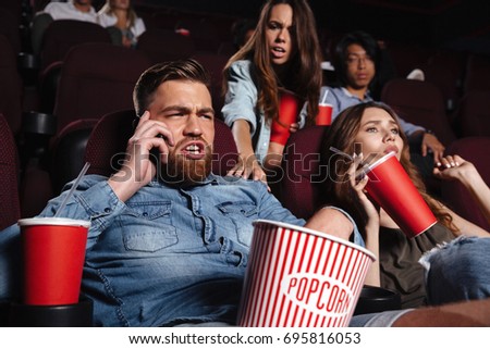 Rude young man talking on mobile phone while watching movie at the cinema and disturbing audience
