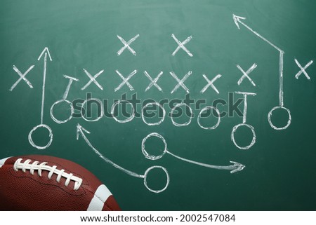 Rugby ball and drawn American football strategy game on green chalkboard, top view