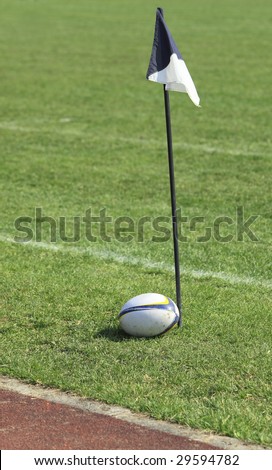 Rugby ball near a flag on the field.There are some intended glare areas on the ball.