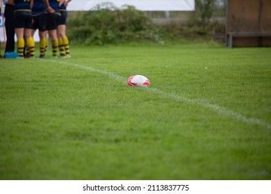 Rugby Ball On Field Before Kickoff. Team Huddling In Background