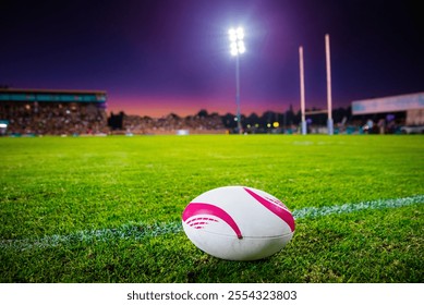 Rugby Match Under Stadium Lights with a Rugby Ball Resting on a Lush Green Field at Sunset, Captivating a Serene Dusk Setting with Illuminated Goalposts for a Thrilling Showdown. - Powered by Shutterstock