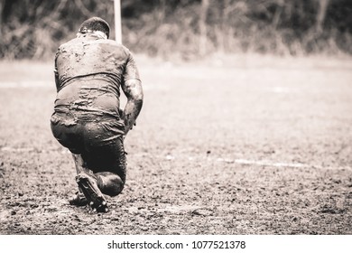 Rugby player covered in mud and kneeling - Powered by Shutterstock