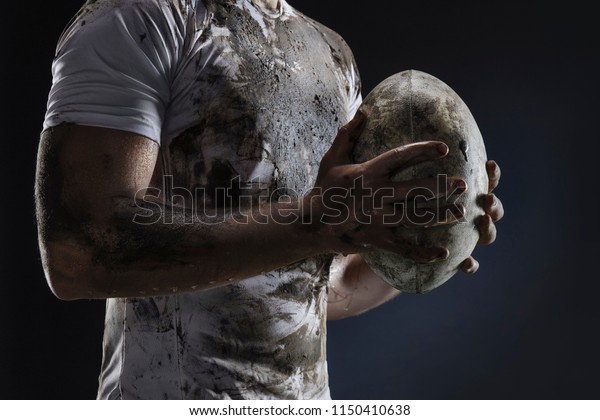 Rugby\
player hands with ball on dark background. Close\
up
