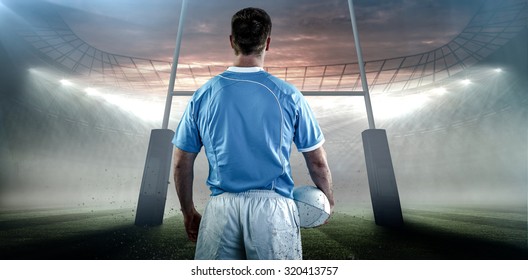 Rugby player holding a rugby ball against rugby stadium - Powered by Shutterstock