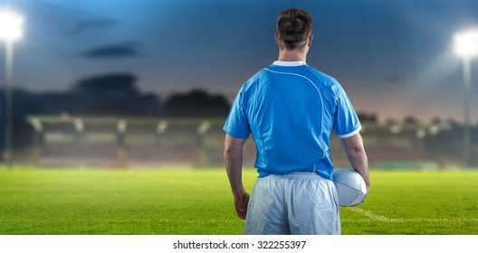 Rugby player holding a rugby ball against pitch - Powered by Shutterstock