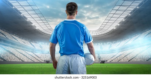 Rugby player holding a rugby ball against soccer stadium - Powered by Shutterstock