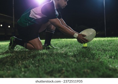 Rugby player placing the ball on tee for penalty shot during the game. Rugby player making a penalty shot under lights at sports arena. - Powered by Shutterstock