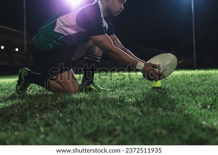 Rugby player placing the ball on tee for penalty shot during the game. Rugby player making a penalty shot under lights at sports arena.