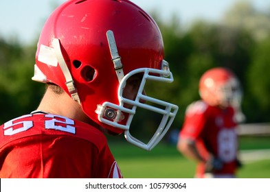 Rugby Player, Side View Rugby Or American Football Player Wearing Red Uniform, Helmet. American Football Team Sport Concept Photo. Sport Background Or Surface With Players In Red Helmet And Uniforms