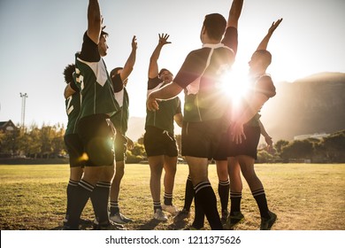 Rugby players celebrating a win at the sports field. Rugby team with hands raised and screaming after victory.
