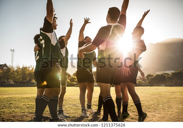 Rugby players\
celebrating a win at the sports field. Rugby team with hands raised\
and screaming after\
victory.