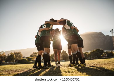 Rugby players standing in a circle with their hands on shoulders. Rugby team in huddle after the match. Bright sunshine through the huddle. - Shutterstock ID 1160436751