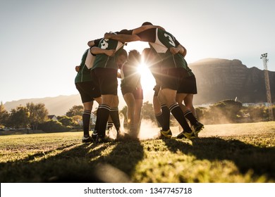 Rugby team standing in a huddle and rubbing their feet on ground. Rugby team celebrating victory.