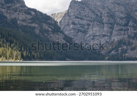 The rugged cliffs and tree lined lower slopes of Prospectors Mountain reflected in the waters of Phelps Lake in Grand Teton National Park 