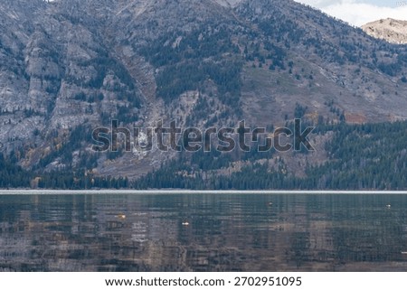 The rugged cliffs and tree lined lower slopes of Prospectors Mountain reflected in the waters of Phelps Lake in Grand Teton National Park 
