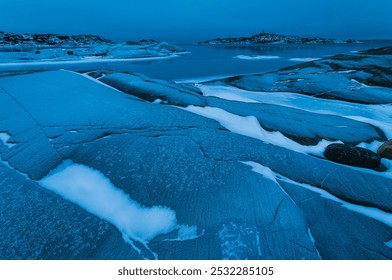 The rugged coastline near Gothenburg, Sweden, reveals smooth, icy rocks and gentle waves under a tranquil blue winter dusk, evoking a sense of peace and solitude. - Powered by Shutterstock