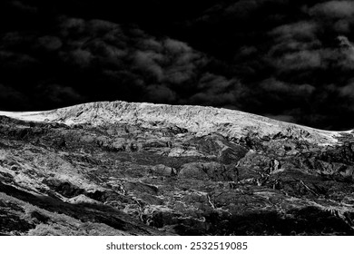 Rugged landscape with jagged, rocky terrain under a dramatic, cloud-filled sky, creating a stark contrast in black and white tones. - Powered by Shutterstock