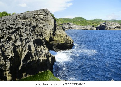 Rugged limestone cliffs meet the deep blue tropical ocean under a clear sky, evoking a sense of powerful natural beauty and serene coastal adventure.