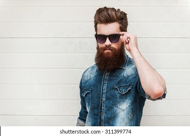 Rugged and manly. Confident young bearded man looking at camera and adjusting eyewear while standing outdoors - Powered by Shutterstock