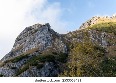 Rugged mountain cliff with green vegetation under clear blue sky on a sunny day. Concept of natural beauty, alpine terrain, and outdoor adventure in a pristine environment. High quality photo - Powered by Shutterstock