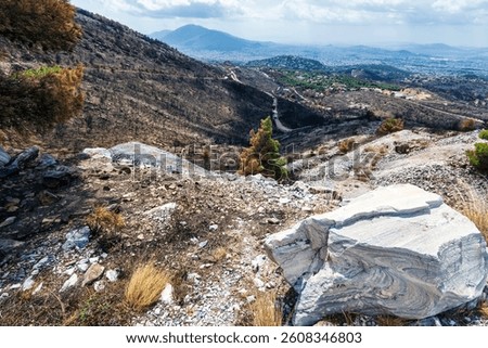 A rugged mountain path curves through scorched hillsides on Mount Penteli, overlooking Athens after the 2024 wildfire devastation.