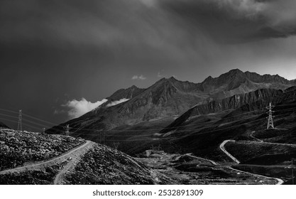 Rugged mountains under dramatic skies, winding roads snake through barren terrain, power lines stretch across landscapes, all in monochrome tones. - Powered by Shutterstock