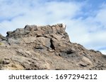 Rugged Outcrop of Volcanic Rock against Blue Sky with White Clouds 