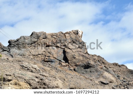 Rugged Outcrop of Volcanic Rock against Blue Sky with White Clouds 