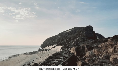 A rugged, rocky cliff overlooking a pristine beach and the vast ocean under a clear blue sky - Powered by Shutterstock