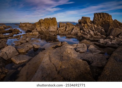 A rugged, rocky shoreline frames a tranquil body of water that gracefully sits in the center of the scene, creating a picturesque view - Powered by Shutterstock