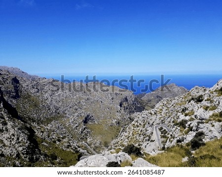 Rugged terrain with sparse greenery under a clear blue sky on Fuerteventura. The landscape features dry rocky hills and arid textures. A depiction of raw, natural, environments in southern Europe.