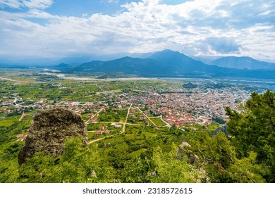 Rugged trees top and big rock in blur view from above of a small town, mountain, river, fields, and houses from afar